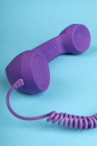 A colorful vintage-style purple telephone handset on a blue background with spiral cord.